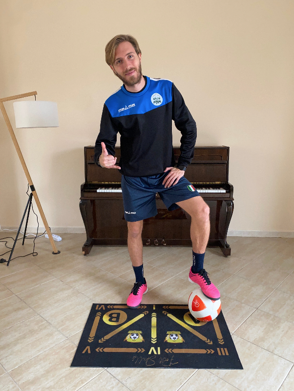 A soccer player posing with a soccer ball on the FootSkills mat, ready to start his technical training at home.